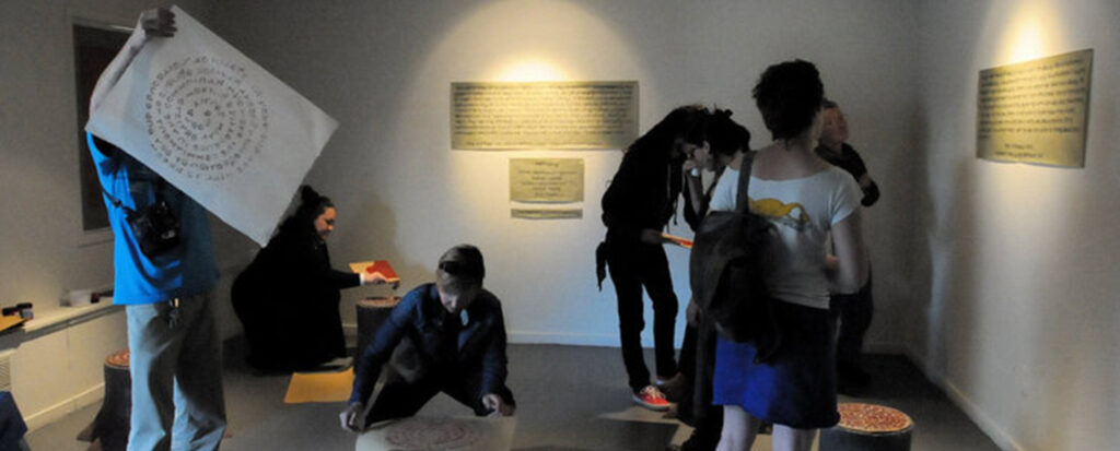 Photo of people in a gallery looking at artwork and holding large sheets of paper